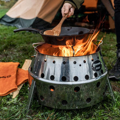 Black cast iron skillet with long handle cooking over a controlled flame in a stainless steel fire pit outdoors, suitable for Farm, Garden & Tool, Camping, Kitchen & Food, Cookware, Cast Iron, Best Sellers, and Promo Eligible collections.