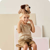 Young child sitting on a wooden stool wearing a soft brown plush dog toy on their head, perfect for Health & Wellness and Children's Toys collections.