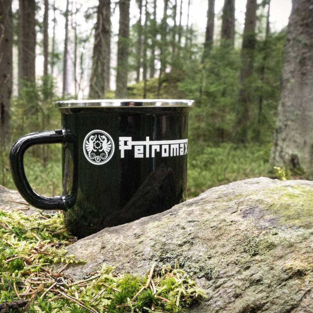 Black enameled steel camping mug with white logo, resting on a mossy rock outdoors in a forest setting, perfect for Farm, Garden & Tool, Camping, and Brewing Coffee and Tea collections.