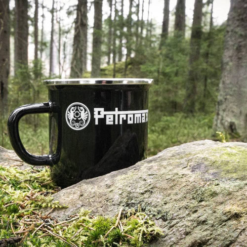 Black enameled steel camping mug with white logo, resting on a mossy rock outdoors in a forest setting, perfect for Farm, Garden & Tool, Camping, and Brewing Coffee and Tea collections.