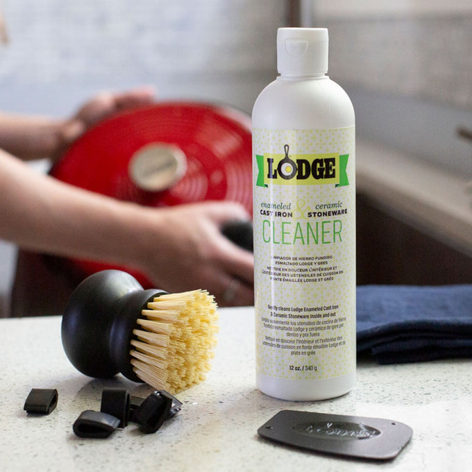 Bottle of biodegradable cleaner for enameled cast iron and ceramic stoneware with a stiff-bristle brush, pan scraper, and black clips on a kitchen counter, part of Kitchen & Food and Cookware collections.