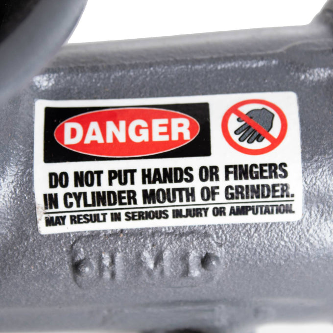 Close-up of a safety warning label on a durable gray metal meat grinder, cautioning against inserting hands or fingers into the cylinder mouth to prevent injury, part of professional Kitchen & Food and Specialty Equipment collections with USA-made quality.