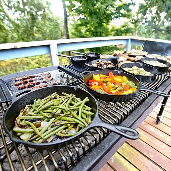 Assorted vegetables and bacon cooking in multiple cast iron skillets on an outdoor grill, highlighting the versatility of Lodge cast iron cookware for Farm, Garden & Tool, Kitchen & Food, Camping, Cookware, Cast Iron, Best Sellers, and Promo Eligible collections.