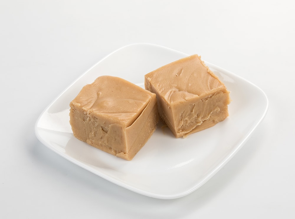 Two handcrafted creamy caramel-colored fudge squares with a rich, melt-in-your-mouth texture on a white plate, featured in Kitchen & Food, Snacks and Sweets, USA Made, Best Sellers, and Promo Eligible collections.