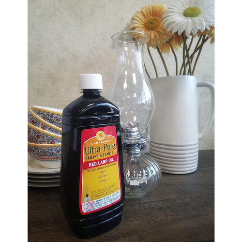 Plastic bottle of red ultra-pure paraffin lamp oil with white cap next to a clear glass oil lamp chimney and ceramic pitcher with flowers, part of Lamps & Lighting and Lamp and Lantern Fuel collections.