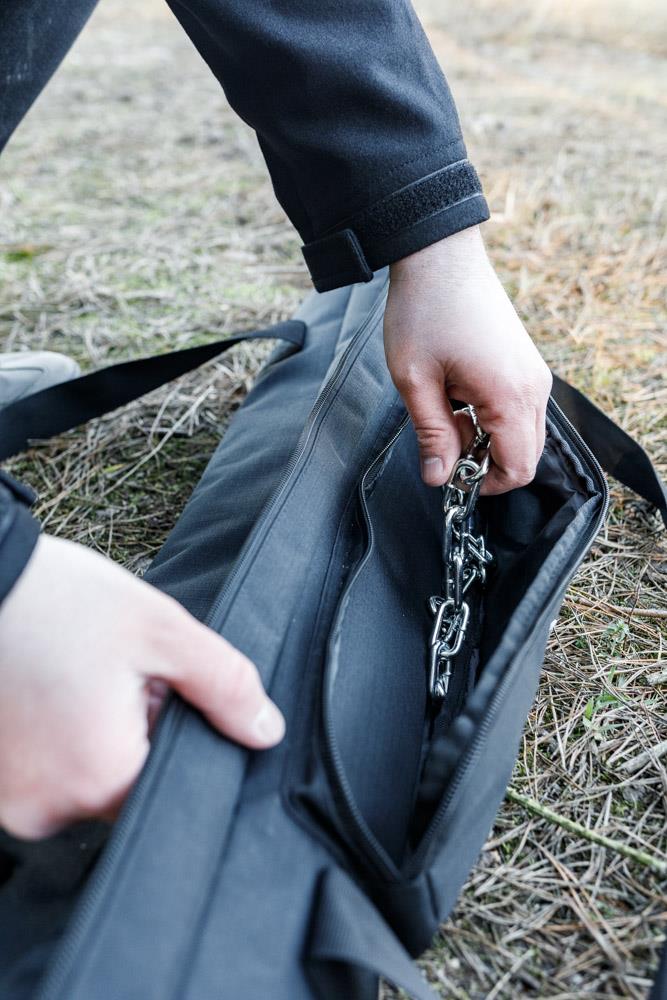 Hands opening a durable black transport bag outdoors, revealing a folded metal cooking tripod inside, designed for use in camping and Farm, Garden & Tool collections.