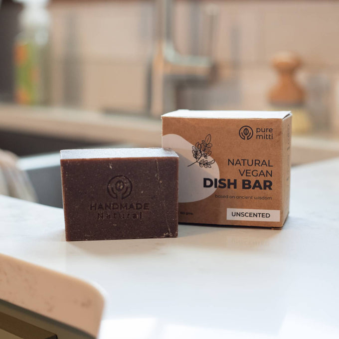 Handmade unscented natural vegan dish bar soap with embossed logo, displayed next to its eco-friendly cardboard box on a kitchen countertop in Home & Decor and Household Cleaning collections.
