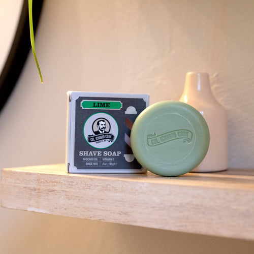 Handcrafted lime shaving soap puck embossed with brand logo, displayed next to its boxed packaging on a wooden shelf, featured in Health & Wellness, Grooming and Personal Hygiene, Soaps and Soapmaking, USA Made, Best Sellers, Promo Eligible collections.