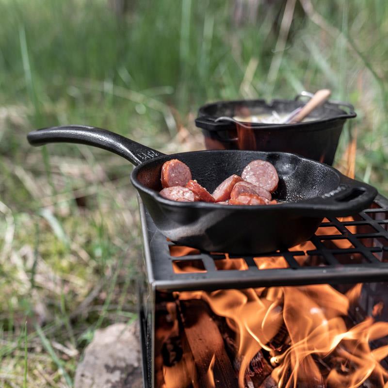 Black cast iron skillet with long handle cooking sliced sausage over an open flame on a portable grill, perfect for Farm, Garden & Tool, Camping, Kitchen & Food, Cast Iron, and Cookware collections.