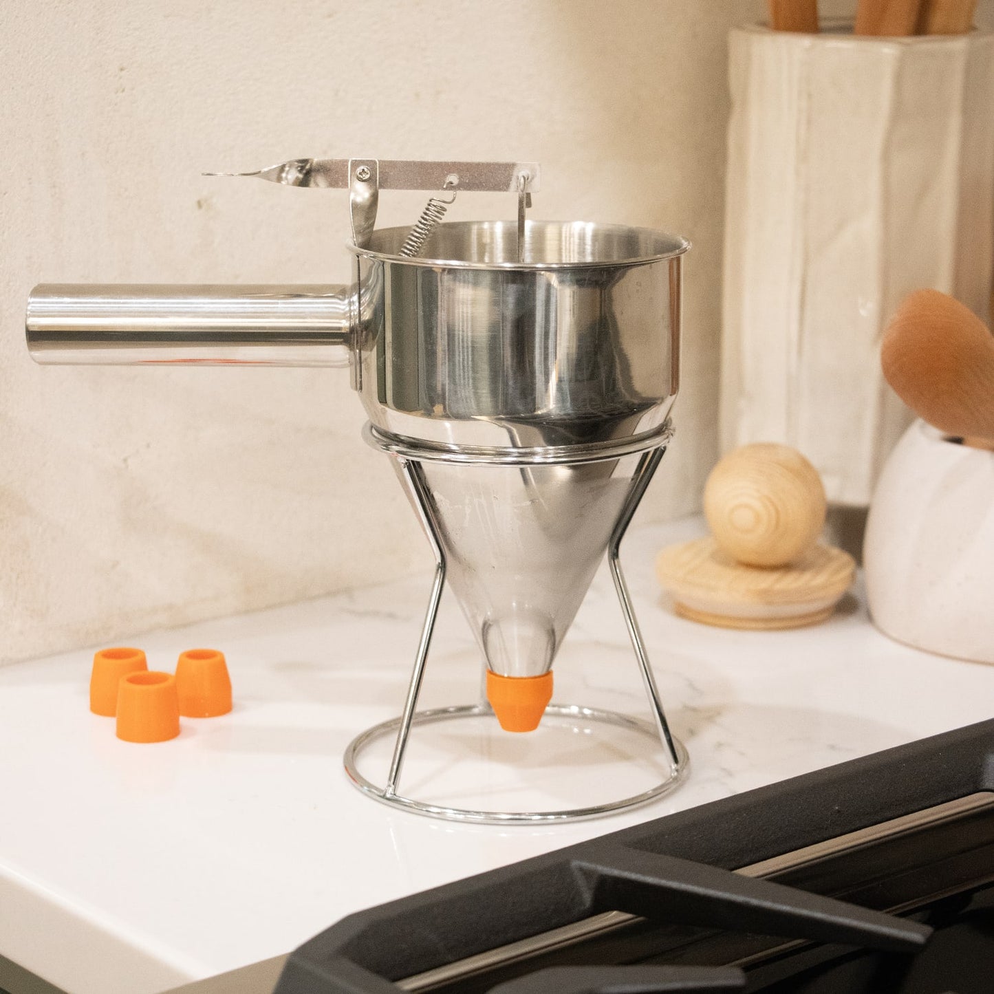 Stainless steel batter dispenser with ergonomic thumb lever and stand, featuring a sealed silicone inner plug and interchangeable orange tips, perfect for Kitchen & Food and Baking Supplies.