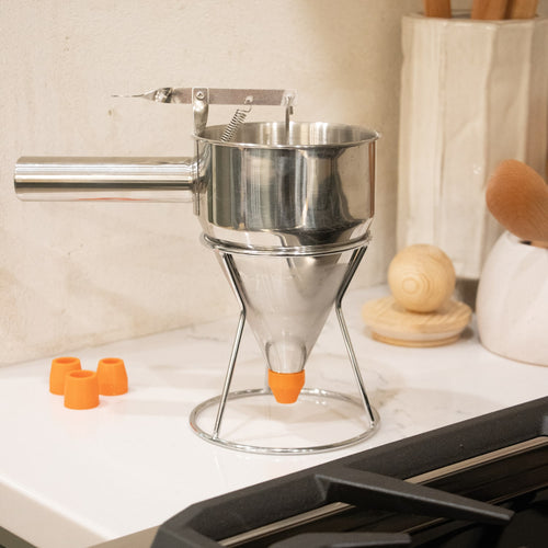 Stainless steel batter dispenser with ergonomic thumb lever and stand, featuring a sealed silicone inner plug and interchangeable orange tips, perfect for Kitchen & Food and Baking Supplies.