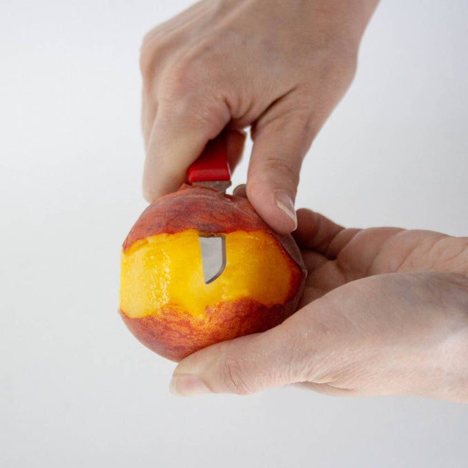 Handcrafted flexible paring knife with a bright red handle peeling a ripe peach, showcasing precise fruit preparation from Farm, Garden & Tool and Kitchen & Food collections.