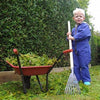 Young child in blue overalls holding a small rake next to a red wheelbarrow filled with green garden clippings, suitable for Farm, Garden & Tool and Lawncare collections.