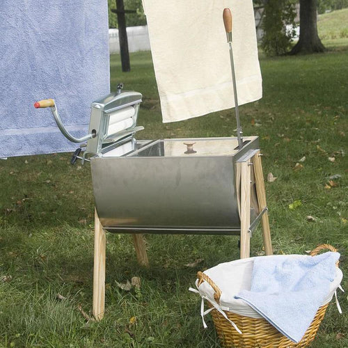 Handcrafted stainless steel laundry washer with wooden legs and manual wringer, set outdoors with hanging towels and a wicker laundry basket, featured in Home & Decor and USA Made collections.