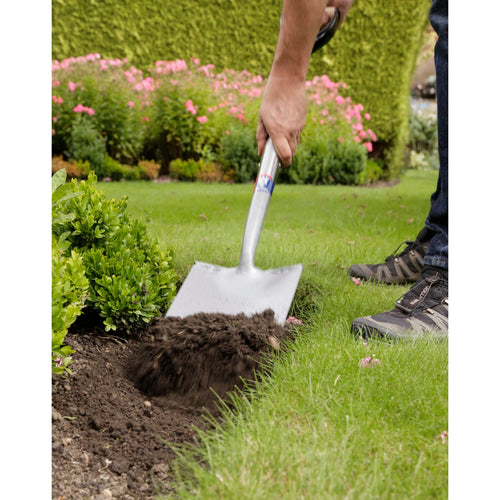 Treaded digging spade with forged carbon steel head used for gardening, digging soil near green shrubs in a lawn setting, suitable for Farm, Garden & Tool and Digging and Cultivating collections.