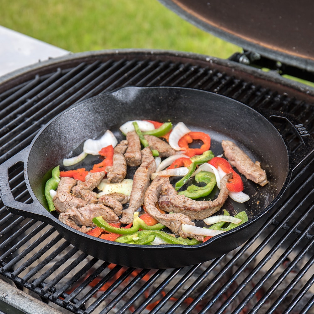 Handcrafted cast iron round pan with short side handles grilling seasoned strips of beef with red and green bell peppers and sliced onions on an outdoor barbecue, featured in Kitchen & Food, Cookware, Cast Iron, Best Sellers, Promo Eligible collections.