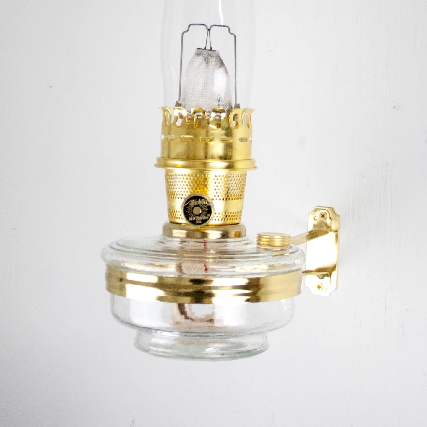 Handcrafted clear glass oil lamp with polished brass burner and wall bracket, designed for mounting classic Aladdin-style lamps, featured in Lamps & Lighting, Oil Lamps, Wall Lamps, Best Sellers, and Promo Eligible collections.