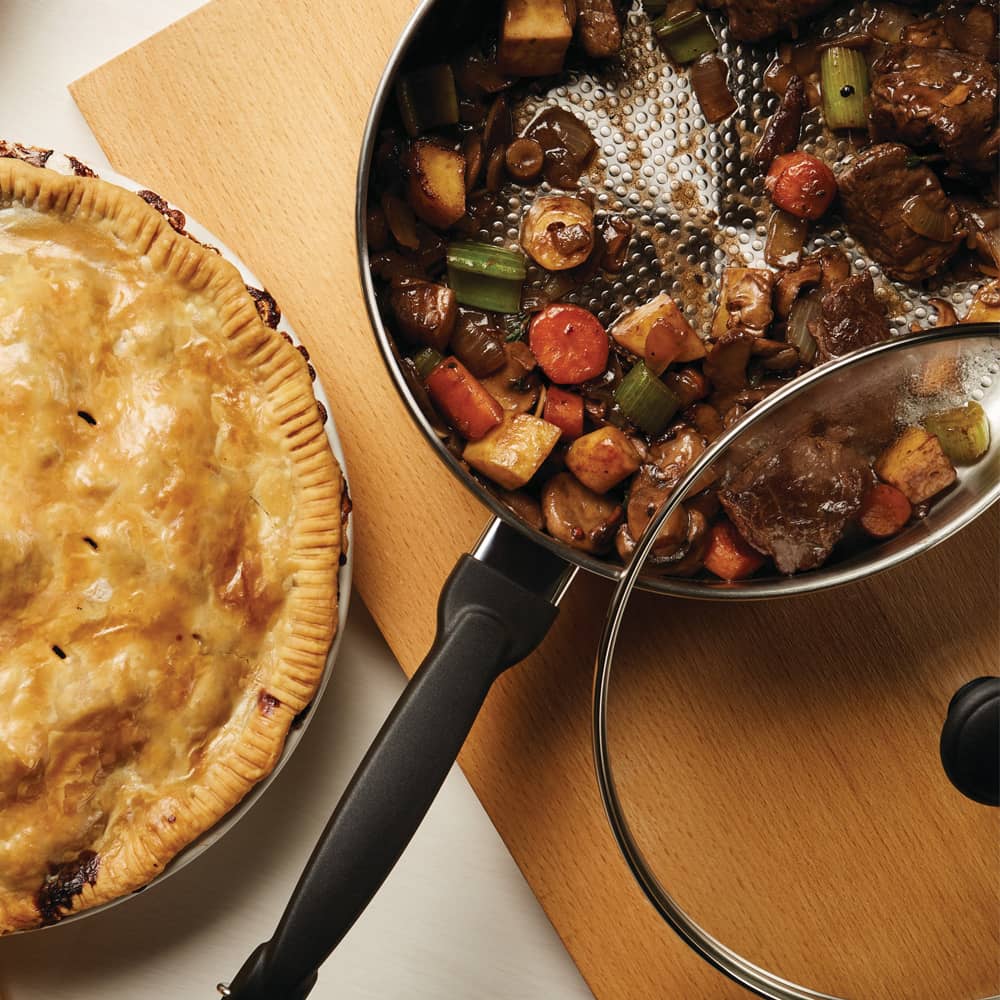 Covered stainless steel saucepot with cooked beef stew including carrots, celery, and potatoes, alongside a golden-brown homemade pie, featured in Kitchen & Food, Cookware, and Best Sellers collections.