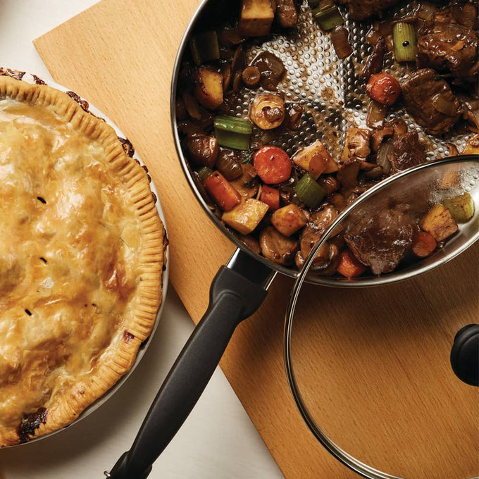 Covered stainless steel saucepot with cooked beef stew including carrots, celery, and potatoes, alongside a golden-brown homemade pie, featured in Kitchen & Food, Cookware, and Best Sellers collections.
