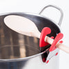 Red and silver pot clip spoon holder securely attached to a stainless steel pot, keeping a wooden spoon elevated and off surfaces, ideal for Kitchen Gadgets and Cooking Helpers.