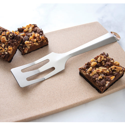 Stainless steel spatula with angled, slotted head resting on a neutral cutting board beside chocolate chip and walnut brownies, handcrafted in the USA, ideal for Kitchen & Food and Storage and Serving collections.