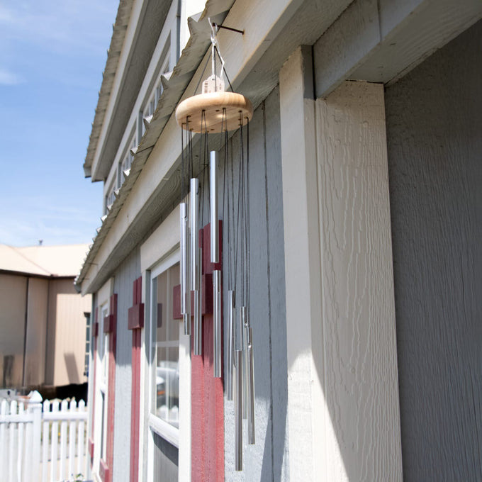 Handcrafted 21" spiral wind chime with silver metal tubes and a wooden top, hanging outdoors on a gray and red building, perfect for garden accessories and farm use.