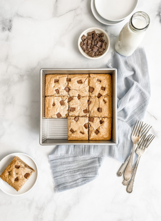 Square baking pan with freshly baked blondies cut into squares, placed on a light gray cloth alongside a bottle of milk, small bowl of chocolate pieces, and vintage forks, ideal for Kitchen & Food, Baking Supplies, and USA Made collections.