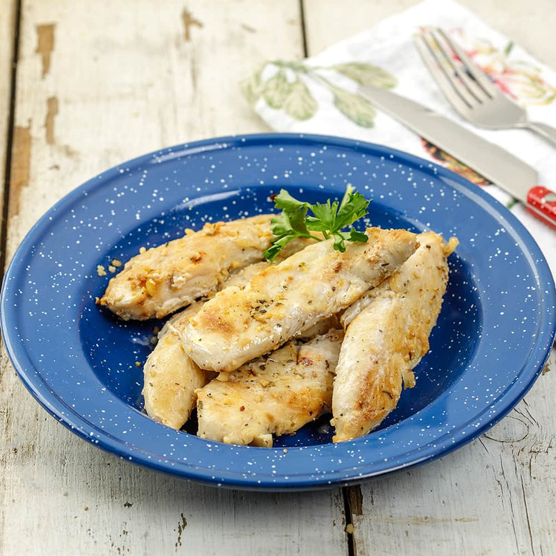 Cooked chicken tenders seasoned and arranged on a speckled blue enamel plate, garnished with fresh parsley, set on rustic wooden surface with cutlery in the background.