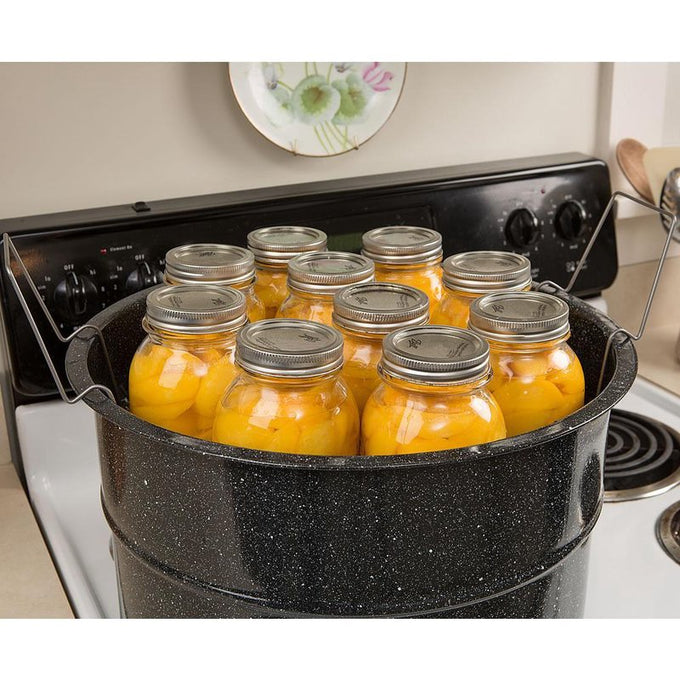 Large black enamelware canner filled with ten sealed glass jars of preserved peaches, set on a stove, ideal for kitchen food preservation and water bath canning tasks.
