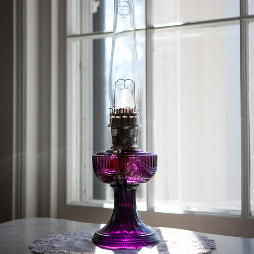 Handcrafted oil lamp featuring a purple Lincoln Drape glass base, clear tall chimney with embossed logo, and brass burner, perfect for Farm, Garden & Tool, Lamps & Lighting, Oil Lamps, Table Lamps, Best Sellers, Homesteading, and Promo Eligible collections.
