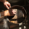 Close-up of hands cleaning a seasoned cast iron skillet with a handcrafted stainless steel chainmail scrubber, set above a kitchen sink, ideal for Farm, Garden & Tool and Kitchen & Food collections.