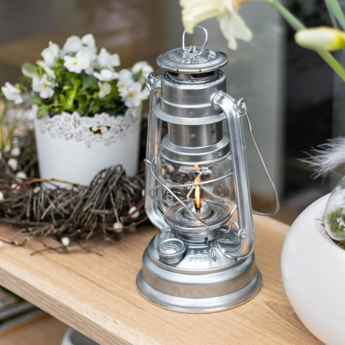 Handcrafted galvanized oil lantern with thermal heat-resistant globe emitting warm light, displayed on a wooden surface surrounded by floral decor, perfect for Lamps & Lighting, Camping, and Emergency Supplies collections.