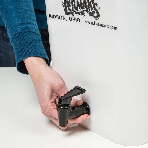 Hand turning the black spigot handle on a sturdy white water filtration bucket, part of a handcrafted Lehman’s filter designed for farm, garden, emergency, and appliance use.