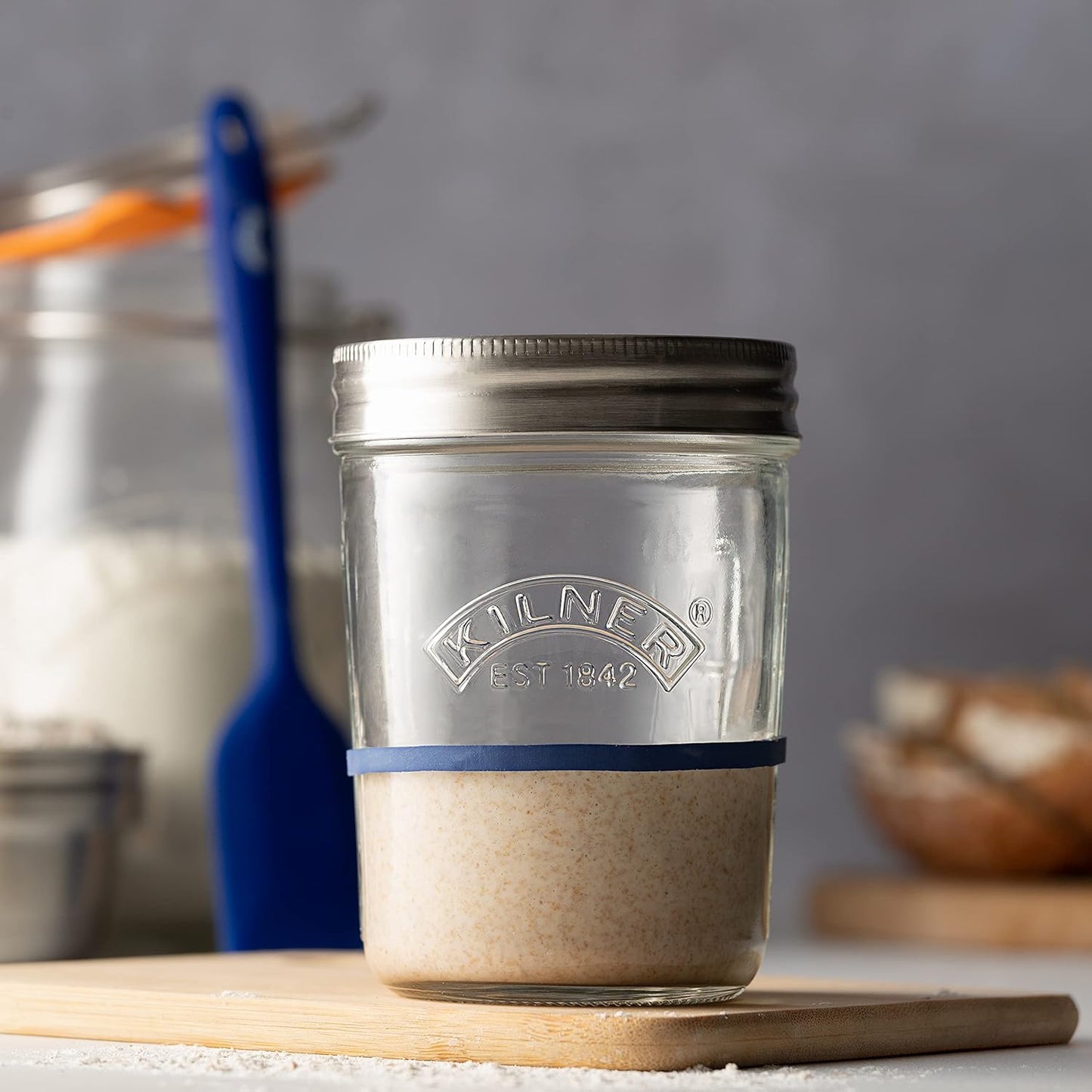 Clear glass jar with metal lid and blue silicone band holding sourdough starter on wooden surface, handcrafted for Baking Supplies, Kitchen & Food, Cookware, and Storage collections.