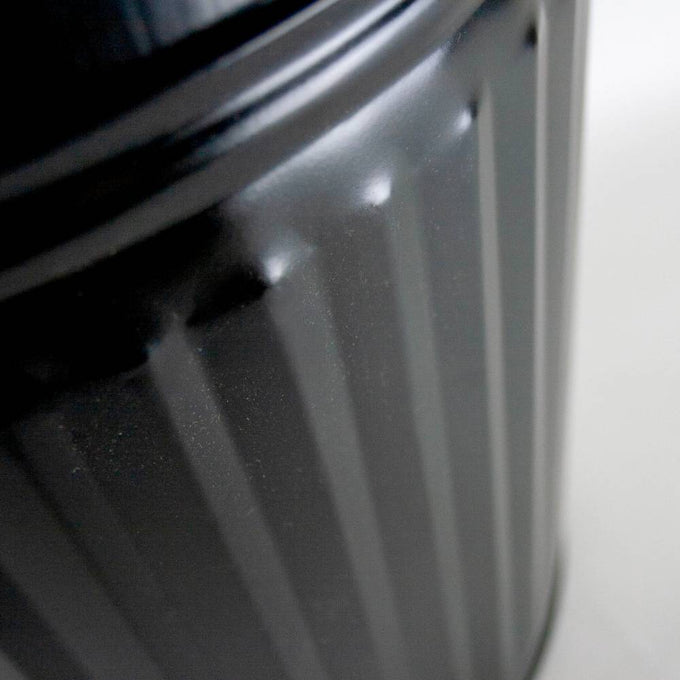 Close-up of a black painted steel pail with vertical ridges, featuring a sturdy design that holds 7-1/2 gallons and is handcrafted for use with stoves and hearth accessories.