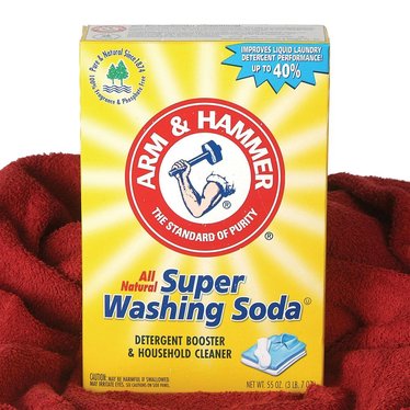 Box of Arm & Hammer Super Washing Soda detergent booster and household cleaner with bright yellow packaging, displayed on a red fabric backdrop, fitting for laundry supplies and home use.