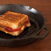 Handcrafted cast iron grill pan with raised ribs and assist handle, showing a grilled sandwich with bacon and tomato, ideal for Kitchen & Food, Cookware, Cast Iron, USA Made, and Best Sellers collections.