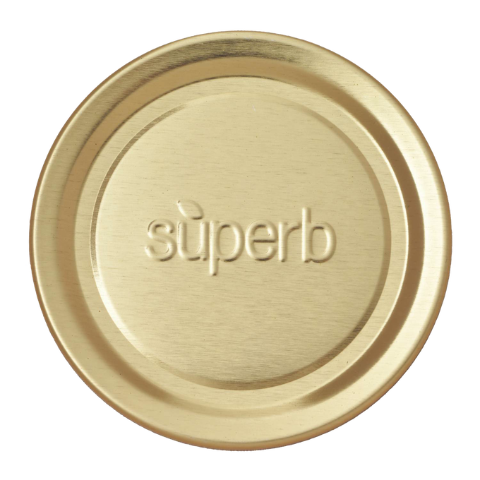 Round metal canning jar lid in a natural brass tone embossed with the word superb, designed for food preservation and kitchen use, part of a USA made collection.