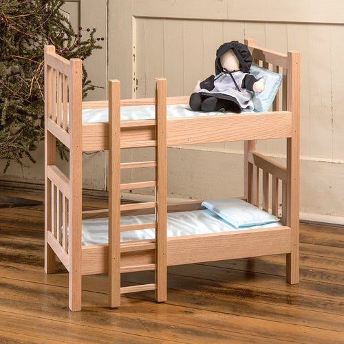 Handcrafted solid oak doll bunk beds with ladder, featuring light blue bedding and a small doll dressed in black and white, perfect for imaginative play and made in USA.