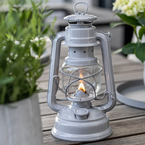Handcrafted galvanized oil lantern with thermal heat-resistant globe, glowing softly on a wooden table surrounded by greenery, ideal for Lamps & Lighting, Camping, and Emergency Supplies collections.