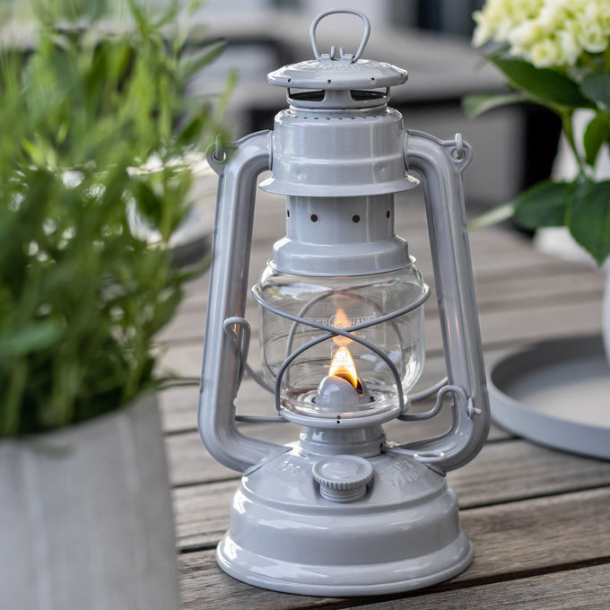 Handcrafted galvanized oil lantern with thermal heat-resistant globe, glowing softly on a wooden table surrounded by greenery, ideal for Lamps & Lighting, Camping, and Emergency Supplies collections.
