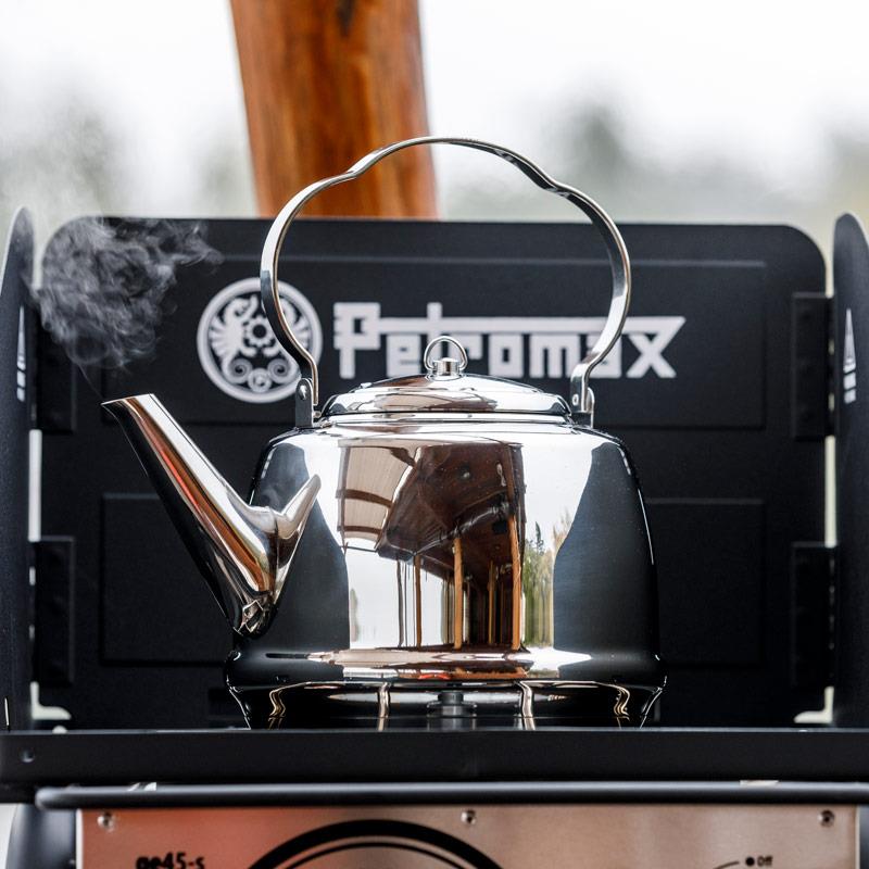 Reflective stainless steel teakettle with a curved movable handle releasing steam, positioned on an outdoor stove, suitable for Farm, Garden & Tool, Camping, and Brewing Coffee and Tea collections.