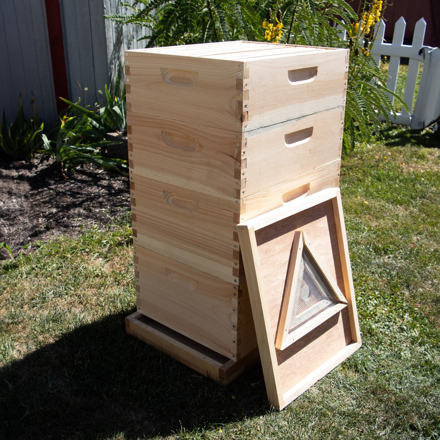 Handcrafted Amish-made wooden beehive with a removable 10-frame triangle bee escape board leaning against it, set outdoors in a garden scene for farm and garden tool collections.