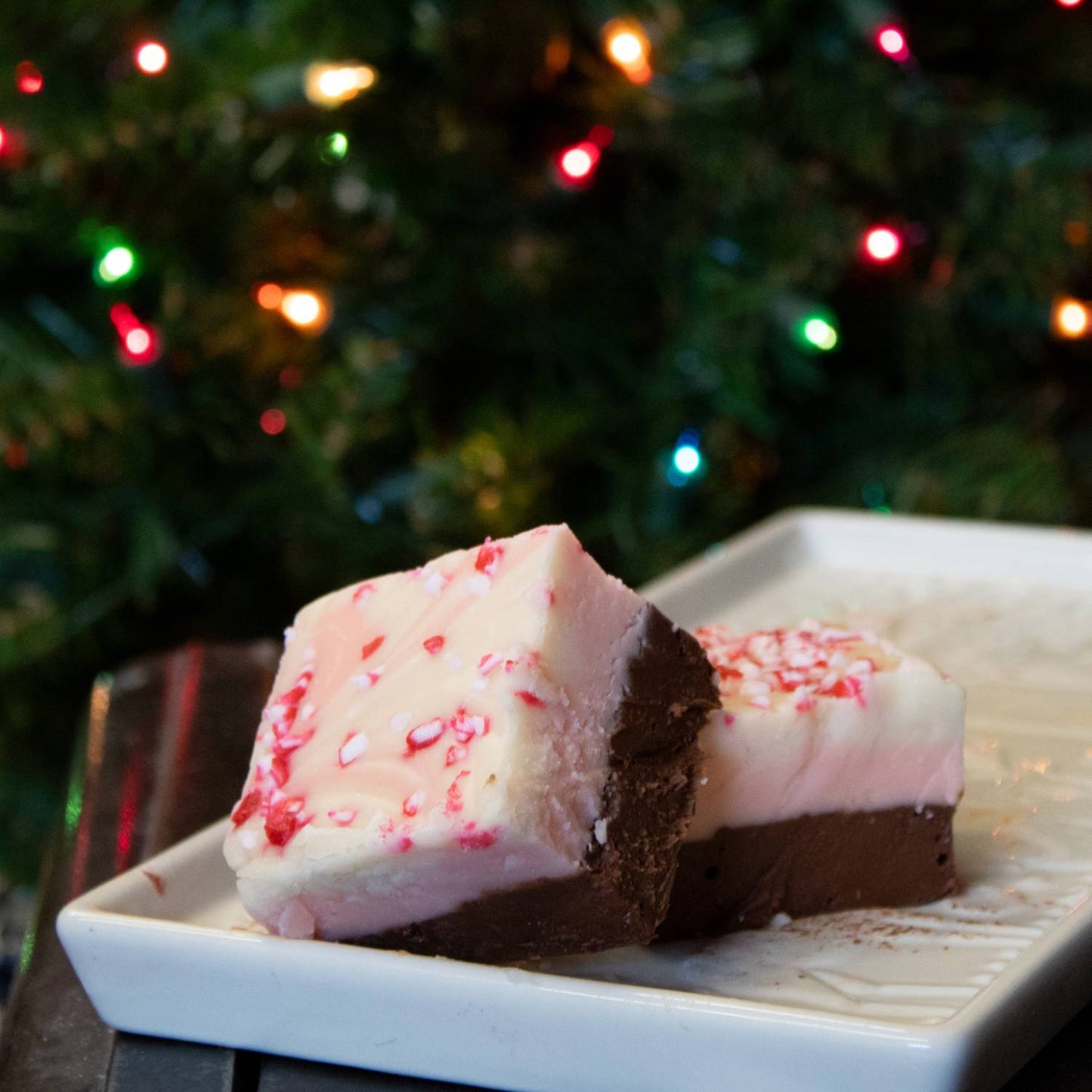 Two handcrafted two-layered fudge pieces with creamy chocolate bottoms and white tops sprinkled with crushed peppermint, set on a white dish, part of Kitchen & Food, Snacks and Sweets, USA Made, Best Sellers, and Promo Eligible collections.