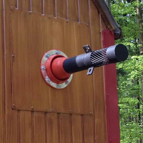 Black metal pipe secured with a red metal flange mounted on a wooden panel of an outdoor structure, surrounded by green forest, suitable for Farm, Garden & Tool and Camping collections.