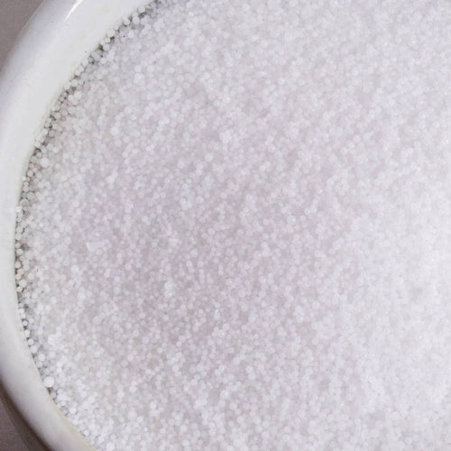 Close-up of small, white high-grade sodium hydroxide lye beads in a white ceramic container, ideal for soapmaking and featured in Health & Wellness, Soaps and Soapmaking, and Soapmaking Supplies collections.