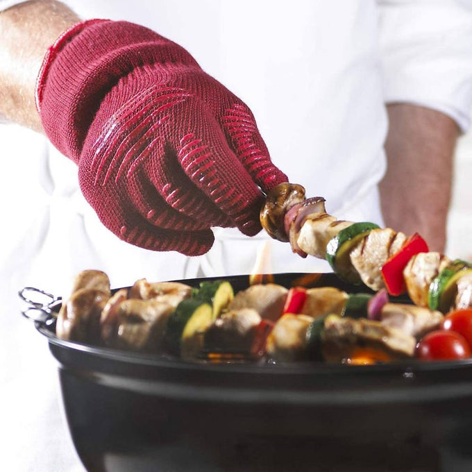Hand wearing a fire-resistant red grill glove with silicone grip, turning vegetable and meat skewers on a charcoal grill, perfect for Kitchen & Food and Grilling collections.