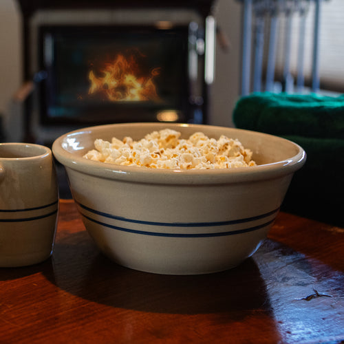 Handcrafted stoneware bowl with blue stripes filled with popcorn, set on a wooden table near a cozy fireplace, featured in Kitchen & Food and USA Made collections.