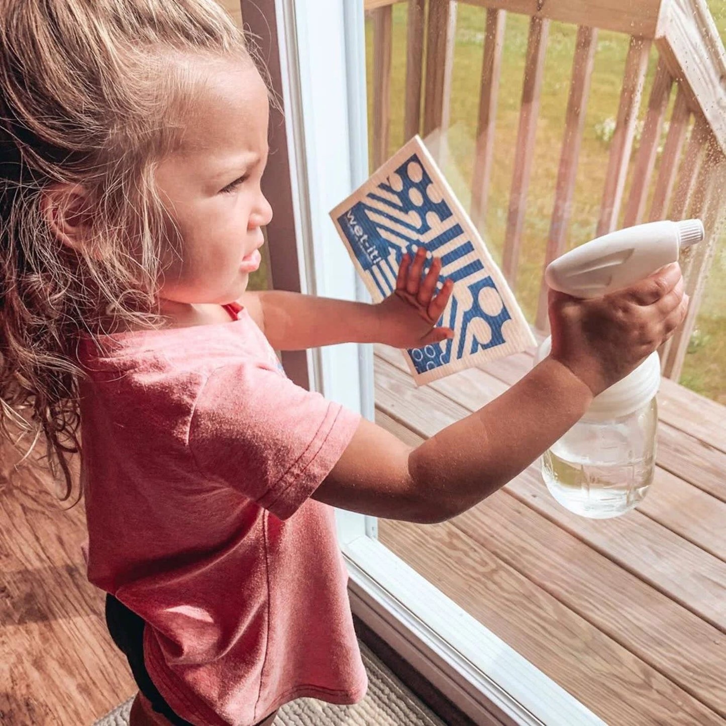 Young child holding a glass jar with a white sprayer lid while cleaning a window, highlighting eco-friendly home cleaning tools from Home & Decor, Household Helpers, USA Made collections.