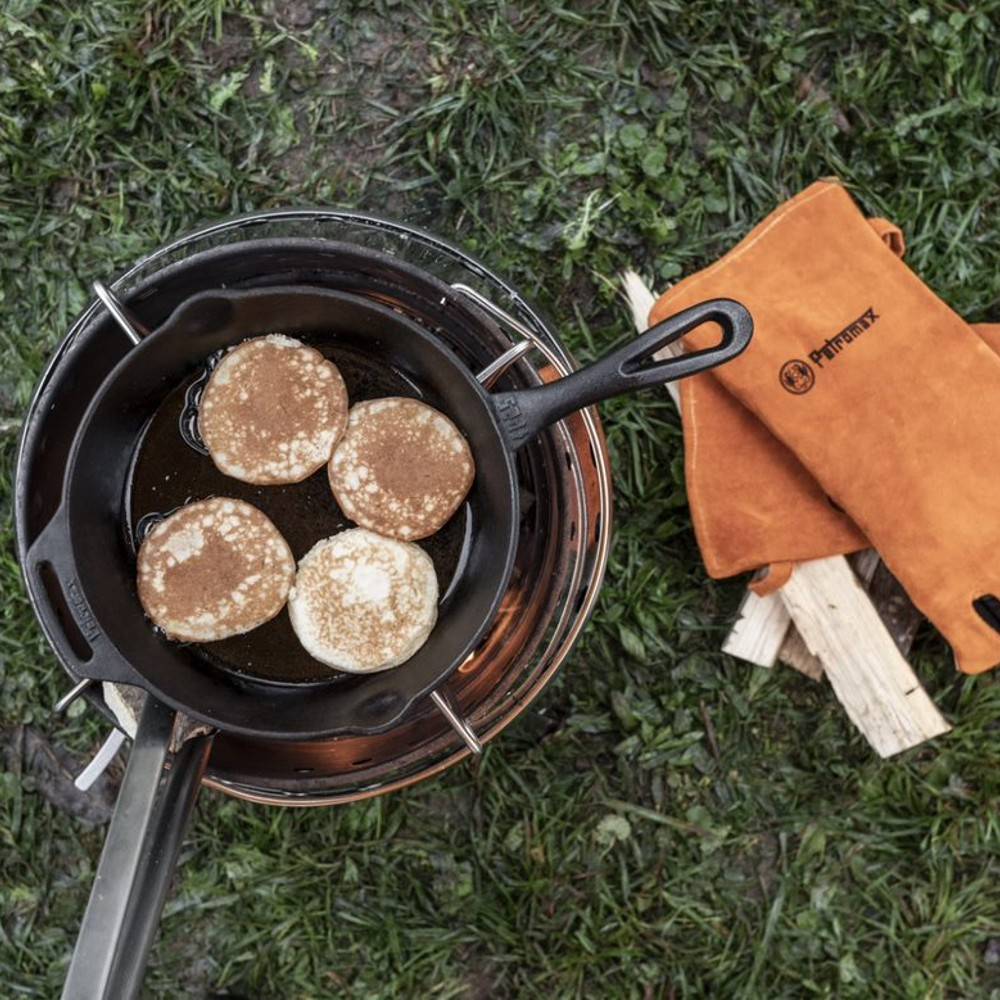 Cast iron Fire Skillet with long handle cooking four golden pancakes over an open flame, next to orange heat-resistant gloves and firewood on green grass, ideal for camping and kitchen use in Farm, Garden & Tool, Kitchen & Food, Camping, Cookware, Cast Iron, and Best Sellers collections.
